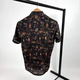 Camisa de manga corta negra con estampado de hojas marrones y logo bordado en el pecho.