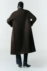 Abrigo largo de corte recto confeccionado en tejido con mezcla de lana, color marrón oscuro. Presenta cuello con solapas, cierre frontal con botones y bolsillos laterales de vivo.