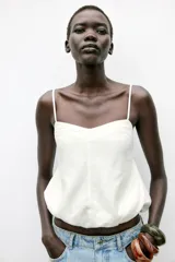 Top corto blanco confeccionado con lino, de tirantes finos, escote pico y espalda abierta con tira elástica horizontal. Tiene bajo abullonado con elástico interior.