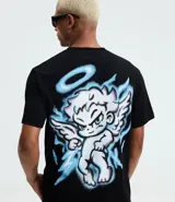 Remera negra de algodón con cuello redondo y mangas cortas. Presenta un estampado frontal con la frase "Divine Spark" y un estampado grande en la espalda de un ángel con halo y rayos celestes.