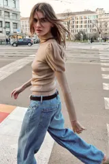 Top de punto en color beige con cuello subido y mangas largas. Presenta un diseño ajustado en el cuerpo con mangas abullonadas en los hombros que combinan una textura semitransparente.