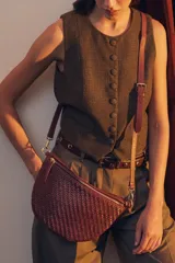 Bandolera de gamuza color marrón con diseño de media luna, decorada con tachas metálicas doradas distribuidas en el frente. Cuenta con cierre superior metálico y correa larga ajustable para llevar cruzada.