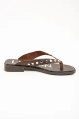 Sandalias planas de cuero marrón tipo ojota con tiras anchas adornadas con tachas metálicas plateadas y plantilla con diseño estampado.