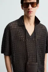 Polo de manga corta confeccionado en tejido de punto calado con estructura abierta. Presenta un diseño de corte relajado, cuello solapa con abertura frontal en pico y terminaciones acanaladas en puños y bajo.