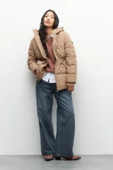 Campera puffer larga color beige, con diseño acolchado horizontal, capucha y bolsillos laterales. Cuenta con cierre frontal con cremallera y solapa con broches a presión, además de puños elastizados y aplique con logo en la manga.