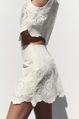 Falda pantalón corta de tiro alto color blanco con bordados florales perforados y forro interior. Cierre lateral con cremallera oculta.