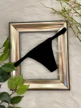 Tanga colaless de color negro, confeccionada en tela suave con detalle de encaje en los bordes superiores y tiras laterales ajustables.