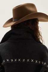 Campera de lana merino hervida en color crudo, con diseño de cuello camisero, cierre frontal de botones y bolsillos frontales. Presenta bordados artesanales con motivos geométricos en tonos marrón y azul en el frente, espalda y mangas.