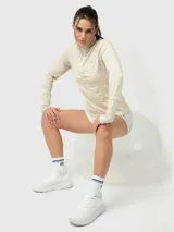 Polera de manga larga color marfil melange, con cuello alto y cierre frontal parcial. Presenta diseño deportivo con costuras visibles y puños con abertura para el pulgar.