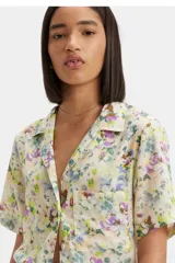 Camisa de manga corta con cuello tipo solapa y cierre frontal de botones. Presenta un estampado floral multicolor sobre fondo claro, corte recto y un bolsillo frontal en el pecho con etiqueta de marca.