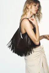 Bolso de hombro tipo shopper, color marrón oscuro, con cuerpo completamente cubierto de flecos largos y asa de hombro delgada. Cierre mediante botón imantado y bolsillo interior con cremallera.
