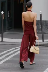 Mono largo de punto color bordó, con escote halter drapeado, hombros descubiertos y detalle de fajín fruncido en la cintura.