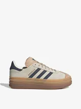 Zapatillas Adidas Gazelle Bold para mujer. Diseño clásico en gamuza color beige con las tres tiras laterales en azul marino. Suela de goma apilada color caramelo.