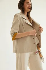 Chaqueta corta de inspiración motoquera color beige, confeccionada en lino fantasía, sin forro, con cierres decorativos, broches de presión y bolsillos delanteros funcionales. Presenta detalle bajo el cuello y en vueltas de mangas en color mostaza y rayas.