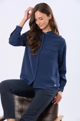 Blusa tipo camisa de manga larga en color azul marino, confeccionada en tela suave y sedosa con doble capa en el frente. Presenta cuello clásico, cierre frontal con botones ocultos y un bolsillo en el pecho.