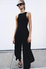Mono largo negro con cuerpo de tejido ajustado sin mangas y cuello redondo, combinado con pantalón ancho de tejido fluido y satinado con diseño abullonado y bajo asimétrico. Cierre trasero con cremallera oculta.