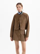 Chaqueta matelaseada color marrón, de corte recto y largo a la cadera, con cuello redondo, cierre frontal con broches dorados y bolsillos plaqué en el delantero.