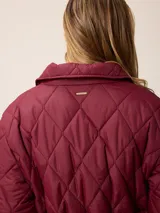 Campera acolchada de diseño matelassé con patrón de rombos, color bordó. Presenta cuello camisero, cierre frontal con cremallera metálica, cintura entallada con elástico y bolsillos laterales. Incluye un pequeño bordado distintivo en el pecho.