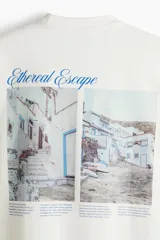 Remera color hueso de corte oversized, confeccionada en tejido de algodón pesado. Presenta cuello redondo acanalado, hombros caídos y estampado pequeño con la frase "Ethereal Escape" en el lado izquierdo del pecho.