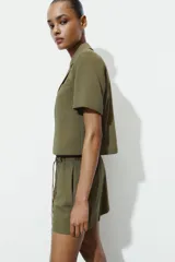 Bermuda de tiro alto en color verde militar, con cintura elástica y detalle de cinturón fino trenzado con abalorios decorativos.