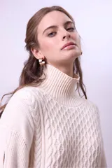 Sweater de punto color bordó con cuello alto y diseño de trenzas en el frente y las mangas. Presenta un corte holgado y largo, con puños y ruedo acanalados.