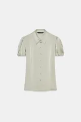 Camisa de satén color verde claro, con cuello solapa, cierre frontal con botones a presión y mangas cortas abullonadas.