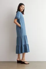 Vestido midi de jean azul, de corte holgado y diseño en capas con volados, escote en V, mangas cortas con detalles bordados en los puños.