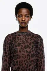 Camiseta de manga larga confeccionada en tejido de tul semitransparente con estampado animal print abstracto. Presenta cuello redondo, corte ajustado y detalles de frunces laterales que aportan textura y movimiento a la prenda.