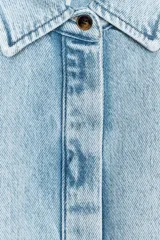 Camisa de denim celeste con cuello solapa, manga corta abullonada y cierre frontal con botones.