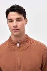 Buzo de punto color azul, con cuello alto y cierre frontal parcial. Presenta un diseño con textura acanalada en los hombros y mangas, y un pequeño bordado en la manga derecha.