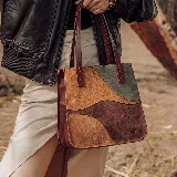 Cartera tipo tote de diseño patchwork, confeccionada en gamuza combinada en tonos tostado, marrón, bordó y verde. Cuenta con doble asa de hombro y detalles de cuero liso en los bordes.