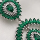Caravanas colgantes de plata 925 con diseño floral y ovalado, adornadas con piedras verdes en forma de marquise y gota, rodeadas de pequeños cristales brillantes.