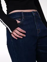 Pantalón de jean color azul oscuro con corte relajado, diseño de cinco bolsillos, cierre de cremallera y botón, y puños enrollados en la parte inferior de las piernas.