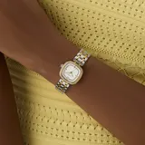 Reloj analógico Guess modelo Hazel con caja cuadrada de 25 mm y correa de eslabones tipo brazalete en acero inoxidable bicolor plateado y dorado. La esfera blanca presenta un marco interno con cristales y el bisel está adornado con cristales brillantes.