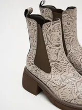 Bota tipo chelsea de cuero vacuno en color rojo con estampado floral grabado en negro. Presenta paneles laterales elásticos, suela de plataforma y taco cuadrado en color negro.