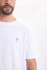 Remera manga corta de color blanco, con cuello redondo y diseño liso. Cuenta con un pequeño bordado de palmera en el pecho.