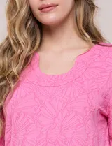 Blusa rosada con textura en relieve de motivos florales, cuello redondo con pequeña muesca y mangas tres cuartos.