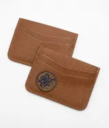 Tarjetero de cuero color suela con textura granulada, cuenta con ranuras para tarjetas y un parche circular bordado con las iniciales de la marca en el frente.