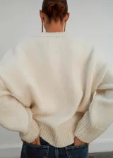 Jersey de punto grueso color blanco, con cuello en V, manga larga y diseño holgado.