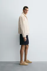 Cazadora de tejido color crema, con cuello alto, cierre frontal de cremallera y bolsillos de vivo en la cadera. Presenta un calce relajado (relaxed fit).