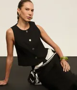 Chaleco de sastrería negro de corte slim, con cuello redondo y cierre frontal de botones metalizados con relieve.