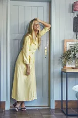 Vestido camisero de largo midi en color amarillo pálido, confeccionado en tejido de cupro. Presenta cuello camisero, cierre frontal con botones y un lazo ajustable en la cintura del mismo material.