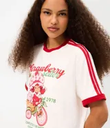 Remera blanca de algodón con mangas cortas, cuello redondo y ribetes rojos en contraste. Presenta estampa frontal de Strawberry Shortcake y lettering con texto en inglés y rojo.