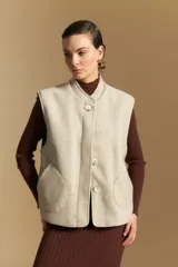 Chaleco de paño color marrón oscuro, de silueta recta y diseño minimalista. Presenta cuello a la base, cierre frontal con botones claros y bolsillos aplicados.