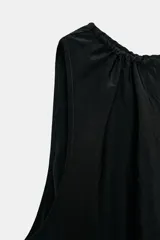 Vestido midi de color marrón con acabado satinado, cuello redondo con detalle fruncido y diseño sin mangas. Presenta un corte fluido con bajo asimétrico y bolsillos laterales ocultos.