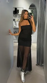 Vestido largo negro de diseño asimétrico con un solo hombro y detalle de choker integrado. Presenta un cuerpo ajustado con frunces laterales y una falda inferior con transparencia en tul, creando un efecto de capas.