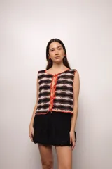 Chaleco tejido a mano en crochet con hilado 100% algodón, con diseño a rayas horizontales en tonos marrón, beige y blanco. Presenta terminaciones en color naranja y lazos del mismo color para cerrar en el frente.