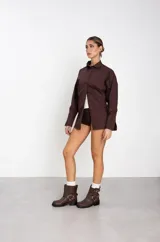 Botas de caña baja en cuero sintético color marrón, con diseño de estilo biker que incluye dos correas horizontales con hebillas metálicas y una argolla decorativa en el lateral. Posee suela y taco bajo de color negro.