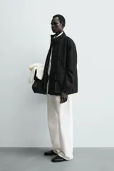 Parka de cuero color negro, de corte relajado, con cuello alto, cierre frontal con cremallera oculta y solapa con botones a presión. Cuenta con bolsillos frontales tipo cargo con solapa en la cadera y bolsillos de vivo en el pecho.