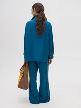 Camisa azul de corte holgado, con cuello camisero, mangas largas con detalles en los puños, bolsillo frontal con bordado y cierre delantero con botones.
